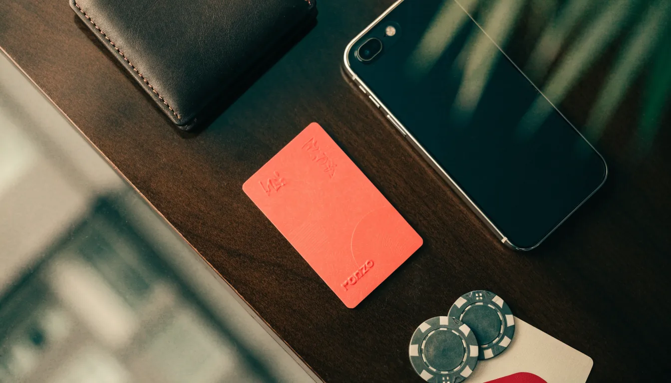 Bank card beside smartphone and subtle casino items on a desk.
